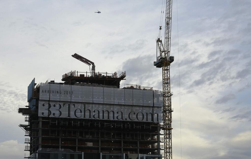 A helicopter flies over a luxury apartment high-rise building under construction on Tehama Street, Wednesday, Feb. 15, 2017, in San Francisco. Several office buildings in San Francisco's South of Market neighborhood have been evacuated after a large unstable concrete slab started tilting and a crane atop the skyscraper malfunctioned on Wednesday. (AP Photo/Eric Risberg)