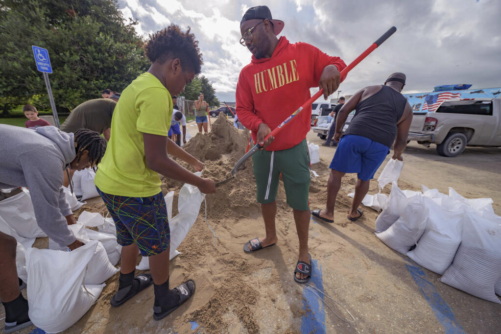 Jawan Williams shovels sand for a sandbag held by his son Jayden Williams, before landfall of Hurricane Ida at the Frederick Sigur Civic Center in Chalmette, La., which is part of the Greater New Orleans metropolitan area, Saturday, Aug. 28, 2021. Hurricane Ida looks an awful lot like Hurricane Katrina, bearing down on the same part of Louisiana on the same calendar date. But hurricane experts say there are differences in the two storms 16 years apart that may prove key and may make Ida nastier in some ways but less dangerous in others..(AP Photo/Matthew Hinton)