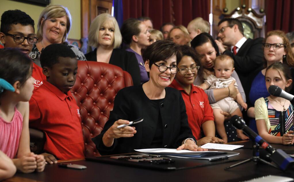 Iowa Gov. Kim Reynolds, center, signs a six-week abortion ban bill into law during a ceremony in her formal office, Friday, May 4, 2018, in Des Moines, Iowa. The bill gives Iowa the strictest abortion restrictions in the nation, setting the state up for a lengthy court challenge. (AP Photo/Charlie Neibergall)