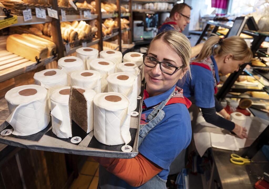 A saleswoman of the bakery Schuerener Backparadies shows a tray with round marble cakes wrapped in fondant that look like toilet paper rolls in Dortmund, Germany, Wednesday, March 25, 2020. The toilet paper cake has become a 'bestseller' during the Corona crisis. (Bernd Thissen/dpa via AP)