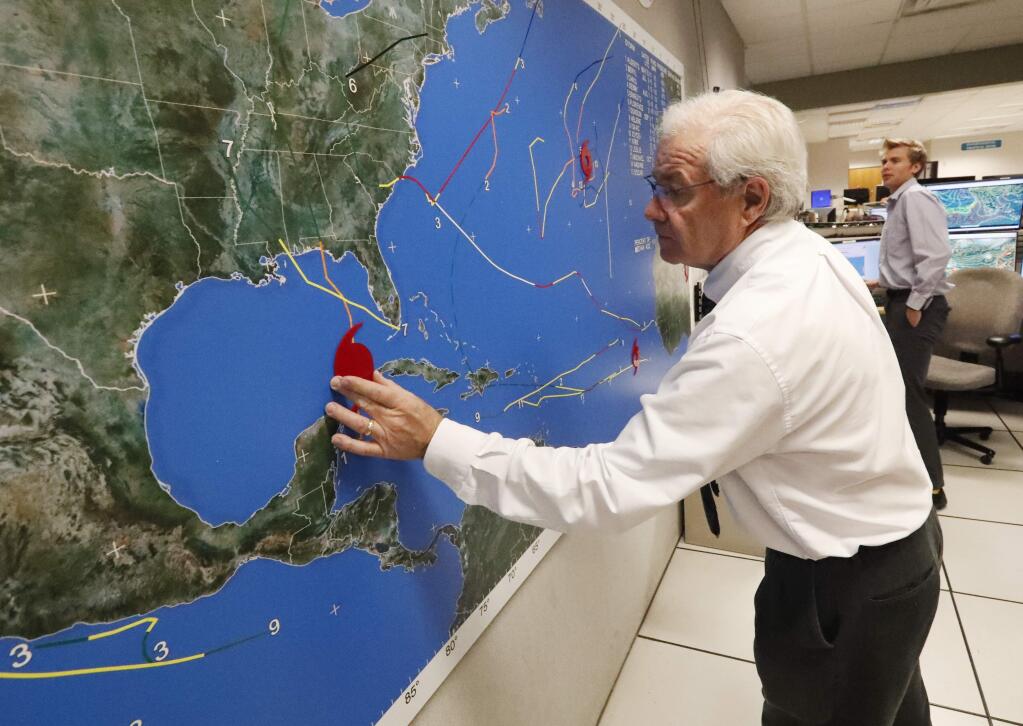 National Oceanic and Atmospheric Administration public affairs officer Dennis Feltgen updates the progress of Hurricane Michael on a large map, Tuesday, Oct. 9, 2018, at the Hurricane Center in Miami. At least 120,000 people along the Florida Panhandle were ordered to clear out Tuesday as Hurricane Michael rapidly picked up steam in the Gulf of Mexico and closed in with winds of 110 mph (175 kph) and a potential storm surge of 12 feet (3.7 meters). (AP Photo/Wilfredo Lee)