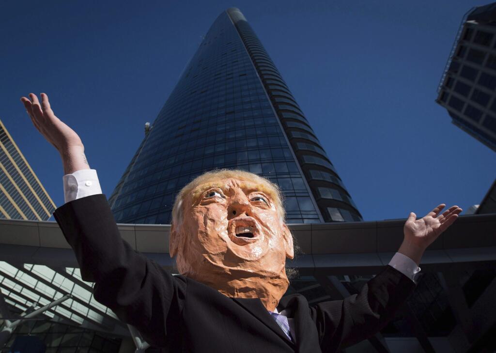 In this Oct. 5, 2016 photo, a man wearing an oversized Donald Trump head protests outside the still under construction Trump International Hotel and Tower, during demonstration in Vancouver, British Columbia, Canada. The 69-story tower has drawn praise for its sleek, twisting design. Prices for the condominiums have set records. But the politics of President Donald Trump have caused such outrage that the mayor won't attend the Feb. 28 grand opening and has lobbied for a name change. (Darryl Dyck/The Canadian Press via AP) /The Canadian Press via AP)