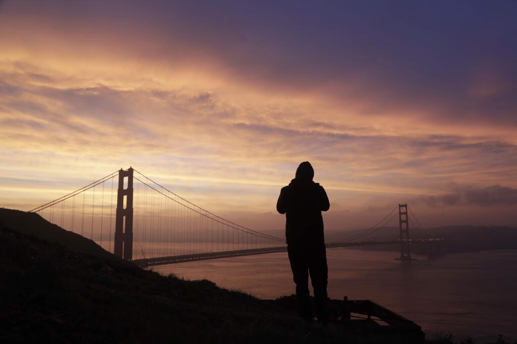 FILE - In this Jan. 17, 2017, file photo, a person photographs the sunrise and the Golden Gate Bridge from the Marin Headlands in San Francisco. Officials say the number of people jumping to their deaths from the Golden Gate Bridge has decreased thanks to the addition of five officers whose job is to spot people trying to commit suicide. (AP Photo/Marcio Jose Sanchez, File)