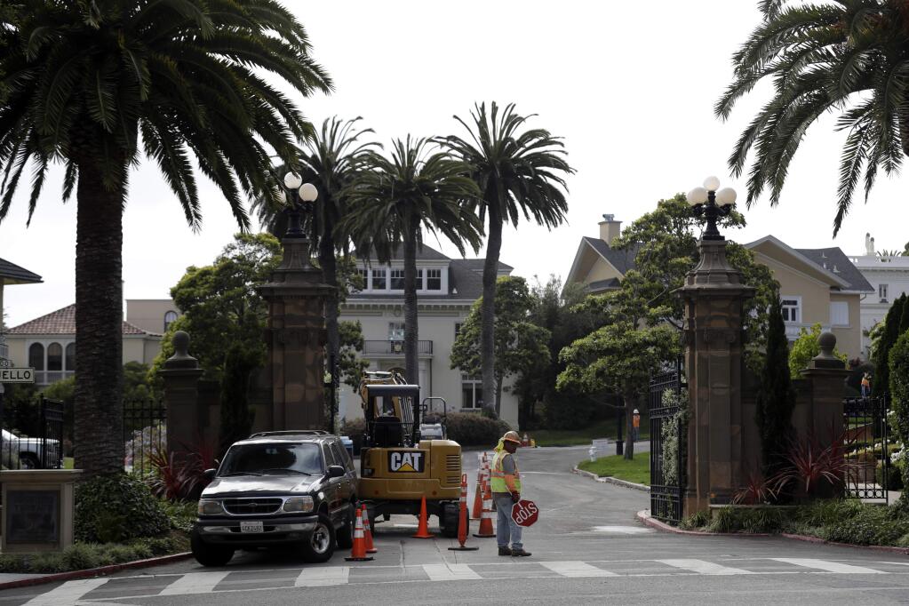 A construction workers stands in front of a gate leading into the Presidio Terrace neighborhood Monday, Aug. 7, 2017, in San Francisco. Thanks to a city auction stemming from an unpaid tax bill, a Bay Area real state investor bought the street in the neighborhood and now owns the sidewalks, the street itself and other areas of 'common ground' in the private development that, the San Francisco Chronicle reports, has been managed by the homeowners association since at least 1905. (AP Photo/Marcio Jose Sanchez)
