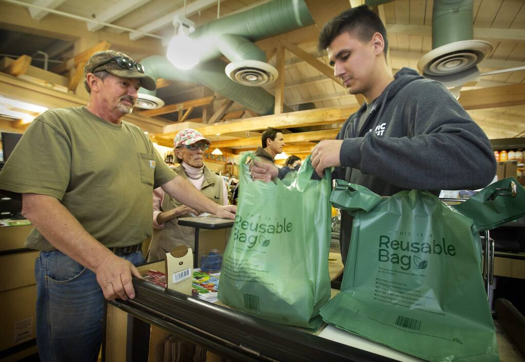 Checker Chris Leach uses a reusable plastic bag for customers Robert Evans, left, and Mary Smith at Pacific Market in Santa Rosa on Friday. (photo by John Burgess/The Press Democrat)