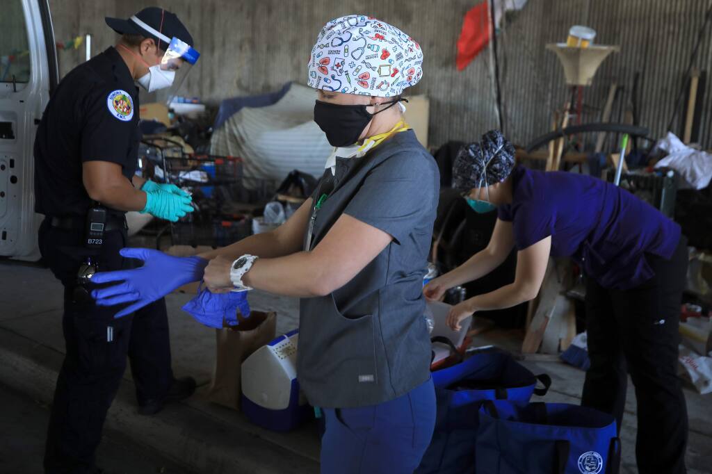 From left, Seth Glover from AMR, Amy Bradbury and Sandra Castano of the Petaluma Health Center, prepare to give test swabs to homeless individuals for the coronavirus, Saturday, June 20, 2020 under Highway 101 at College Ave. In Santa Rosa. (Kent Porter / The Press Democrat) 2020