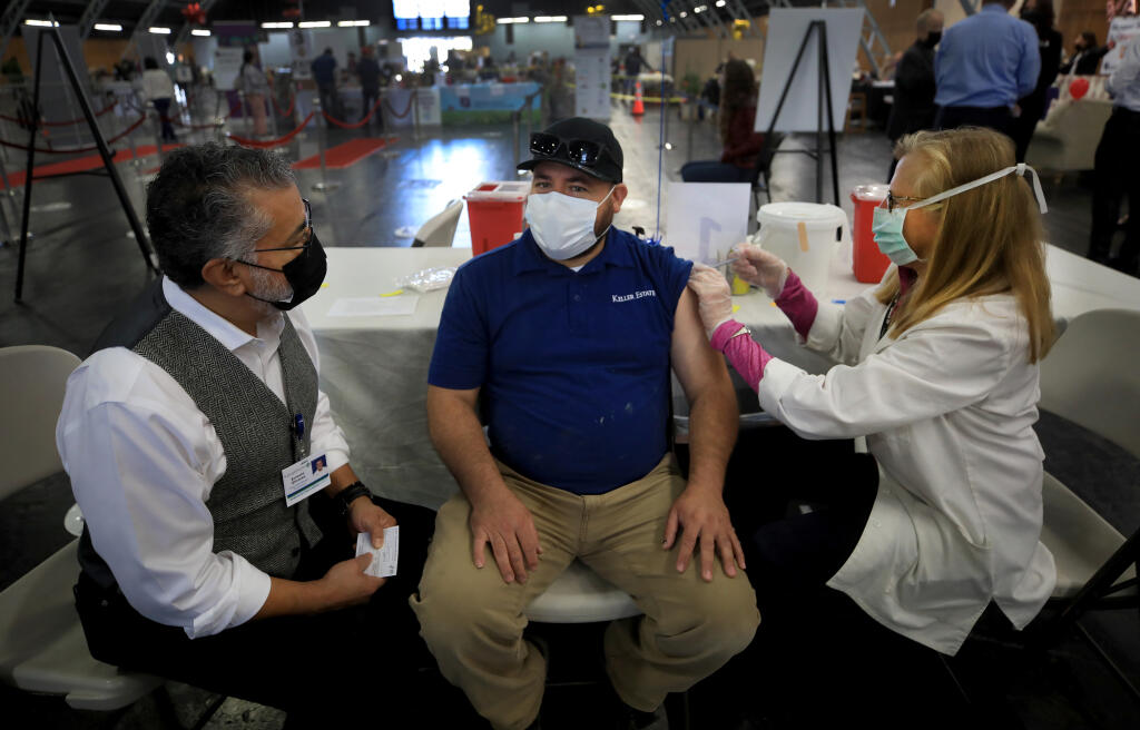 Dr. Loie Sauer vaccinates vineyard worker David Dominguez of Healdsburg, during the Sonoma County Medical Association's vaccine clinic at the Sonoma County Fairgrounds, Friday, March 19, 2021 in Santa Rosa. At left, Ernesto Olivares, St Joseph’s public affairs manger,  volunteers his time to interpret. (Kent Porter / The Press Democrat) 2021