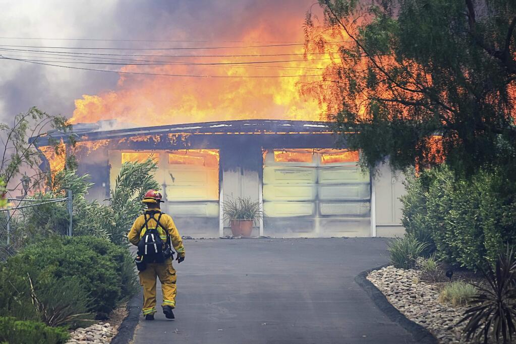 A firefighter approaches a burning home along Olive View Road during a wildfire Friday, July 6, 2018, in Alpine, Calif. Gusty winds fanned the flames as Southern California struggles through a scorching heat wave. (Eduardo Contreras/The San Diego Union-Tribune via AP)