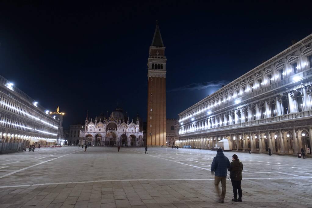 People walk in an almost empty St. Mark's Square in Venice, Italy, Monday, March 9, 2020. Italian Premier Giuseppe Conte says he is restricting travel  nationwide to try to stop the spread of the new coronavirus. Conte said Monday night a new government decree will require all people in Italy to demonstrate they need to work, have health conditions or other limited legitimate reasons to travel outside their home areas. (Anteo Marinoni/LaPresse via AP)