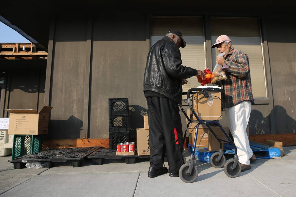 Redwood Empire Food Bank volunteer Pedro Miras helps Alonzo Smith, a homeless senior, fills up a box with food at the Rohnert Park Senior Center in Rohnert Park on Wednesday, Nov. 14, 2018. (BETH SCHLANKER/ The Press Democrat)