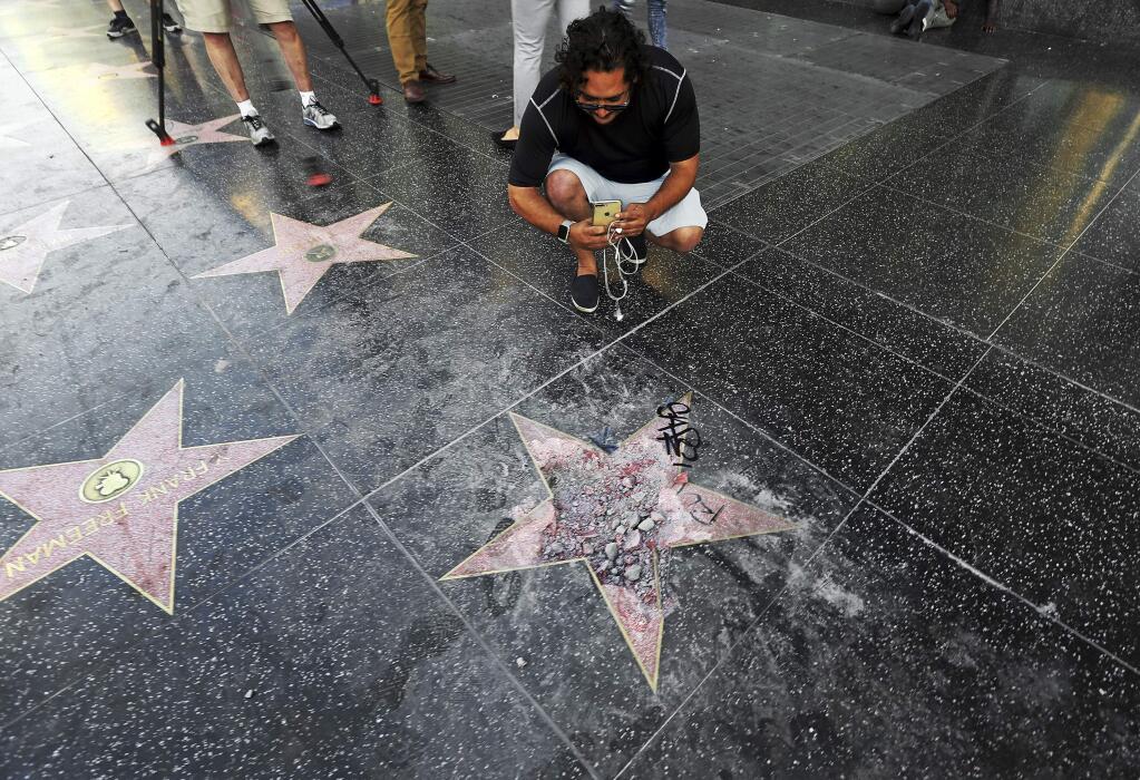 Victor Lomelli of Los Angeles blogs over the vandalized star of Donald Trump on the Hollywood Walk of Fame Wednesday morning, July 25, 2018, in Los Angeles. Authorities say the vandalism was reported around 3:30 a.m. Wednesday and someone was subsequently taken into custody. The star placed on Hollywood Boulevard near Highland Avenue in 2007 recognizes Trump for his work on the reality show 'The Apprentice.' (AP Photo/Reed Saxon)