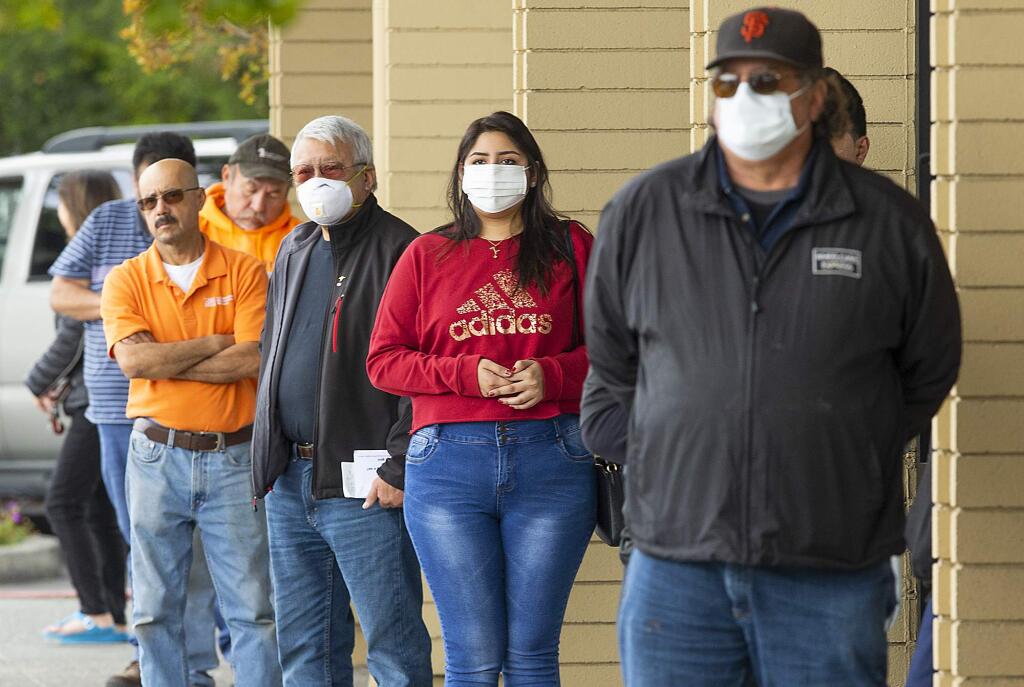 Customers line up 6 feet apart while waiting in line to get into the Wells Fargo Bank branch on Cleveland Ave. in Santa Rosa on Monday. The Centers for Disease Control has recommended people wear protective face masks when out in public. (photo by John Burgess/The Press Democrat)