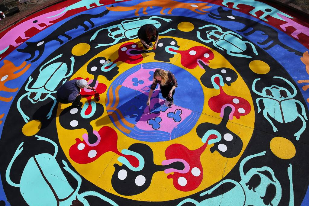 An artist who goes by the pseudonym Bud Snow, lower right, paints her mandala mural with the help of Judy Kennedy, left, and Reina Rivera at Juilliard Park, in Santa Rosa, on Wednesday, February 10, 2016. The mural was commissioned by the Santa Rosa Art in Public Places Committee with a grant from Downtown Connect.(Christopher Chung/ The Press Democrat)
