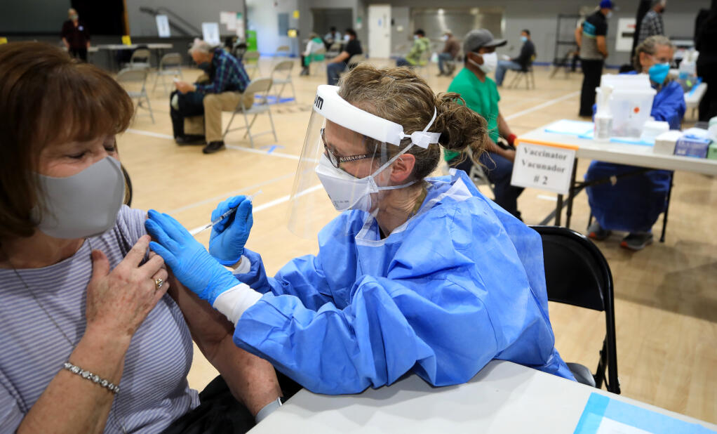 Jessica Williams, a volunteer RN from Guerneville, vaccinates Sharon Zimmerman with her second Moderna vaccine.  In the background right, Christine Fox, also a volunteer RN, prepares to vaccinate another patient, Saturday, Feb. 27, 2021 at Guerneville Elementary School.  (Kent Porter / The Press Democrat) 2021