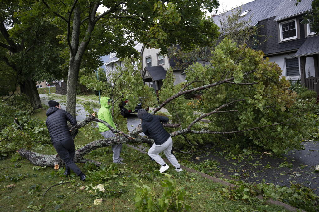 People work to drag a fallen tree limb from their street as post tropical storm Fiona causes widespread damage in Halifax on Saturday, Sept. 24, 2022.  Strong rains and winds lashed the Atlantic Canada region as Fiona closed in early Saturday as a big, powerful post-tropical cyclone, and Canadian forecasters warned it could be one of the most severe storms in the country's history. (Darren Calabrese /The Canadian Press via AP)
