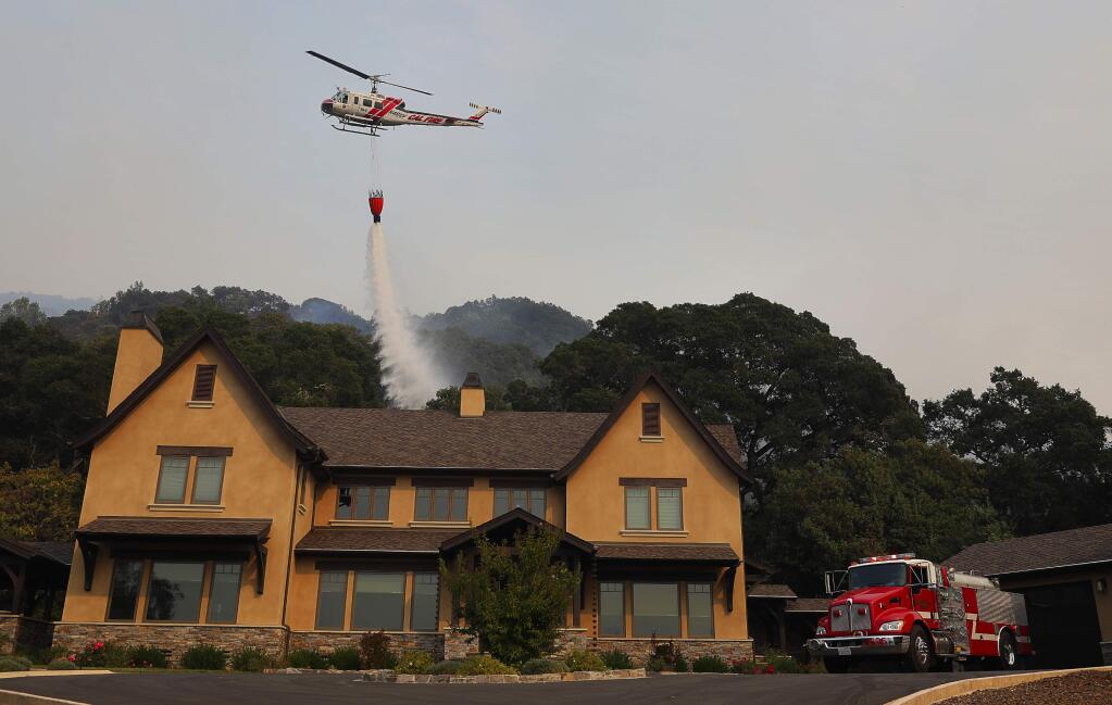 A Cal Fire helicopter drops water Wednesday to protect a structure along Bennett Valley Road near the intersection of Grange Road, near Santa Rosa on Oct. 11, 2017. (Christopher Chung/ The Press Democrat)