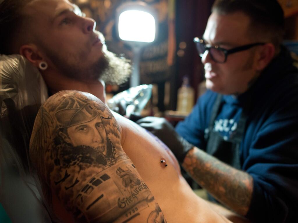 Rory Heilman, left, has a tattoo of his grandfather, a World War II pilot, on his shoulder and gets a new one of an owl across his chest by artist Cody Holyoak of Aces Over Eights Tattoo during Izzy's 23rd annual Santa Rosa Tattoos and Blues in Santa Rosa, Calif., on March 1, 2014. (Alvin Jornada / The Press Democrat)