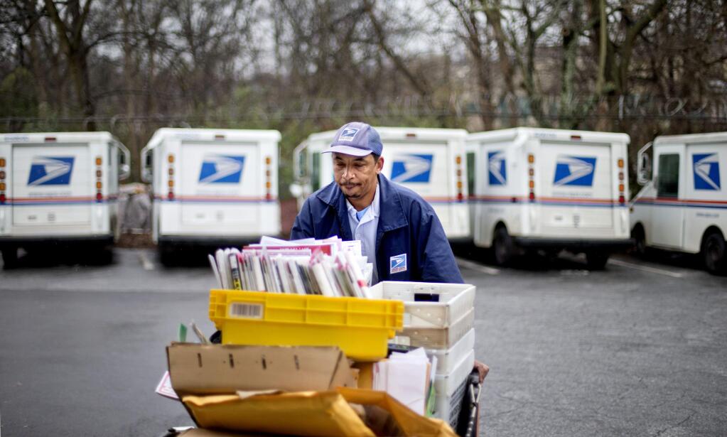 In this Feb. 7, 2013 file photo, a U.S. Postal Service letter carrier gathers mail to load into his truck before making his delivery run in the East Atlanta neighborhood in Atlanta. (AP Photo/David Goldman, File)