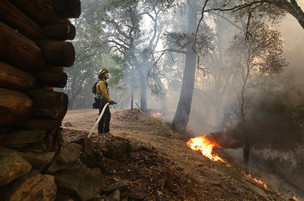 Cal Fire firefighter Nicolas Camello watches fire climb uphill while protecting a wooden barn along Old Lawler Toll Road near Calistoga on Friday, Oct. 2, 2020.  (Christopher Chung/ The Press Democrat)