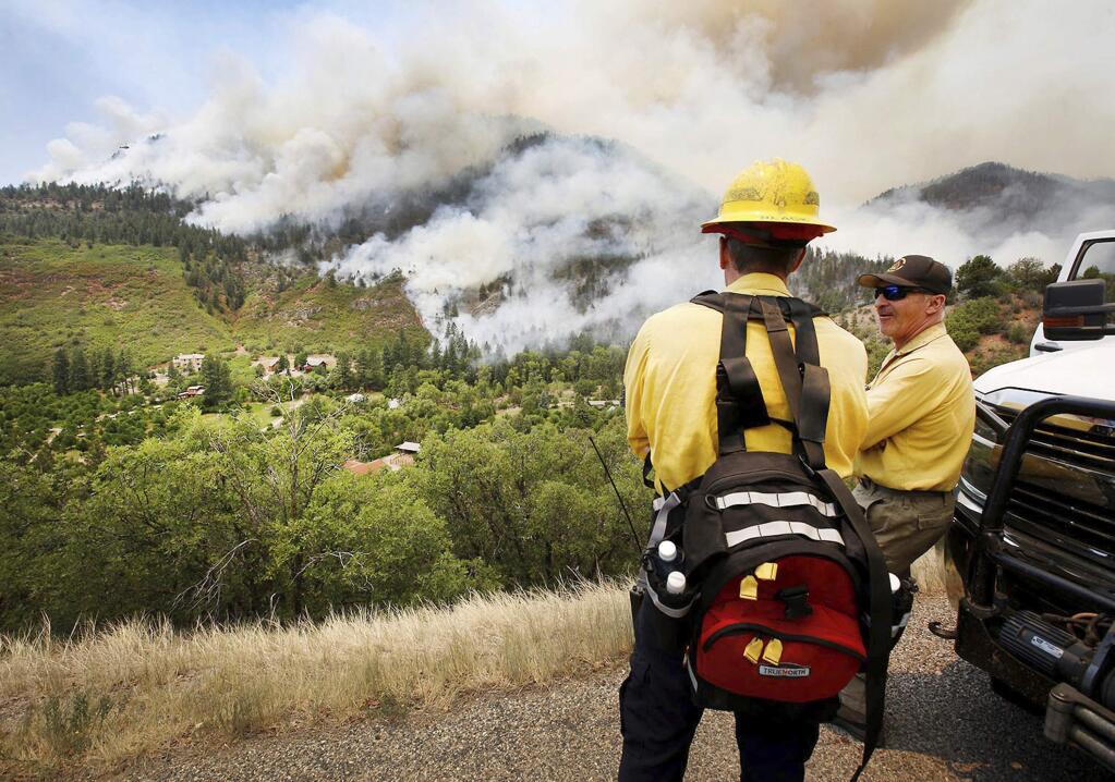 In this Monday, June 11, 2018, photo, Randy Black, left, deputy chief of Durango Fire Protection District, and Mike Tombolato, a Rocky Mountain Type One Team member, look over as a fire burns around homes south of County Road 202 during a burnout operation, a technique used to consume fuel from a growing wildfire, near Durango, Colo. (Jerry McBride /The Durango Herald via AP)