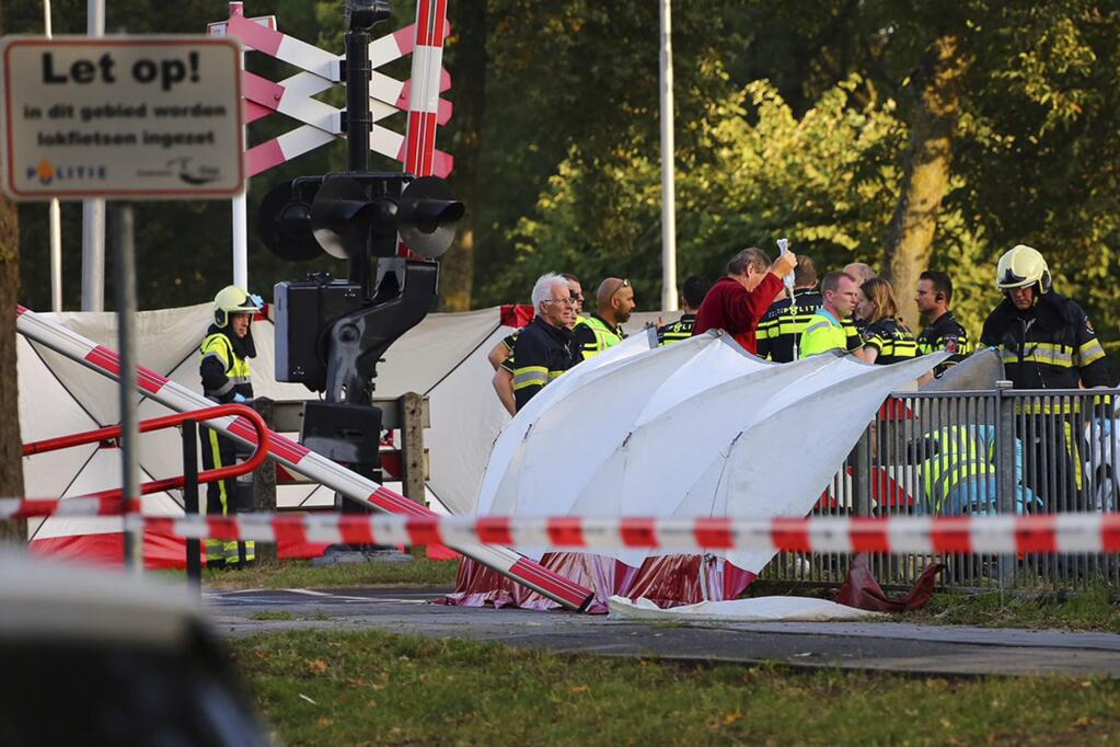 Rescue workers tend to victims of a collision on a railway line, next to a sign in Dutch, left, reading 'Warning, in this area cargo bikes are being used' in Oss, Netherlands, Thursday Sept. 20, 2018. Dutch police say that four children have been killed and two people seriously injured in a collision between a train and a cargo bike. (AP Photo/Charles Mallo) NOT FOR USE IN THE NETHERLANDS, NO SALES, MANDATORY CREDIT