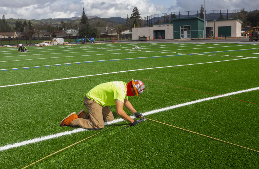 Workers measure for different colored striping to accommodate football, soccer and la crosse on the new Sonoma Valley High School playing field behind the high school on Friday, March 19, 2021. The new clubhouse is in the background. (Photo by Robbi Pengelly/Index-Tribune)