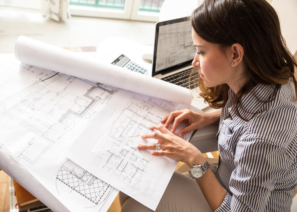 A female architect works at home, looking at blueprints. (BalanceFormCreative / Shutterstock)