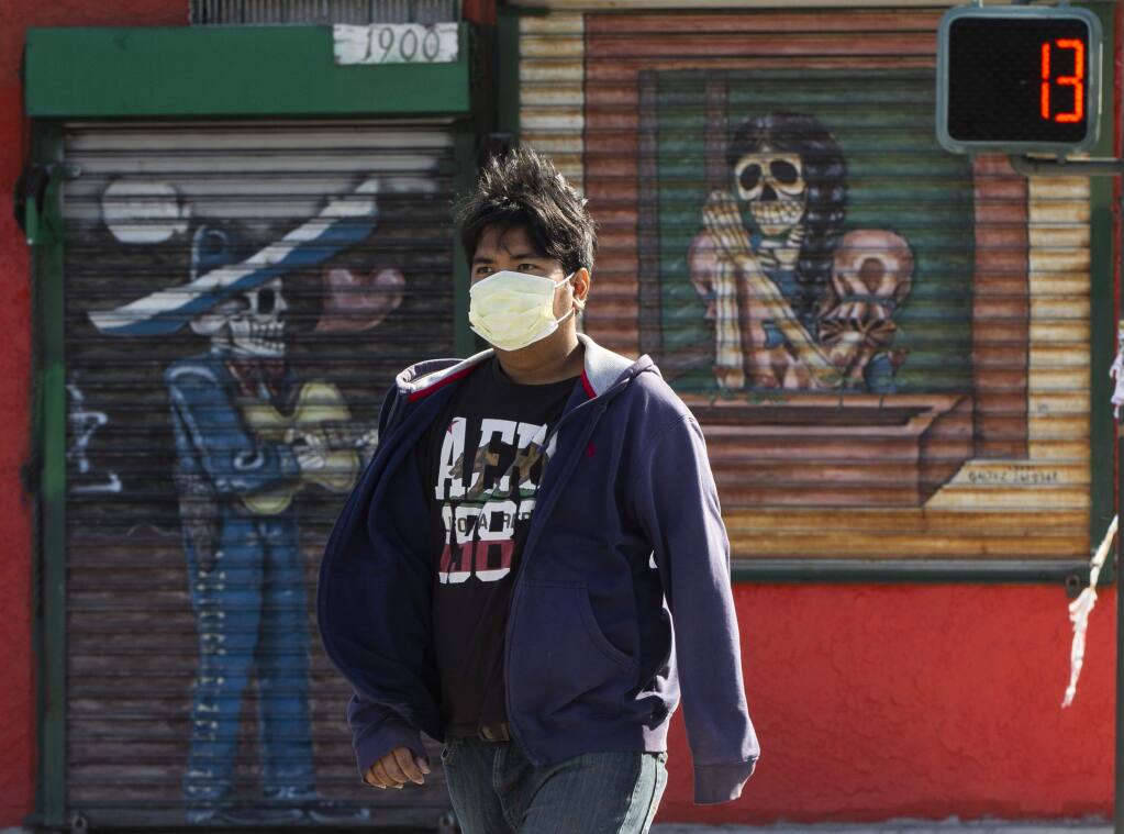 A pedestrian wears a face mask in the Boyle Heights area of Los Angeles on Wednesday, April 1, 2020. Public health officials in California are recommending people wear masks when going outside amid the spreading coronavirus. . (AP Photo/Damian Dovarganes)