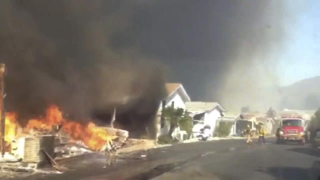 In this video grabbed image released by the San Diego Fire Department Strike Team @SDFD shows a row of homes burning in the Lilac fire in Bonsall, Calif. A brush fire driven by gusty winds that have plagued Southern California all week exploded rapidly Thursday north of San Diego, destroying dozens of trailer homes in a retirement community and killing race horses at an elite training facility. (San Diego Fire Department via AP)