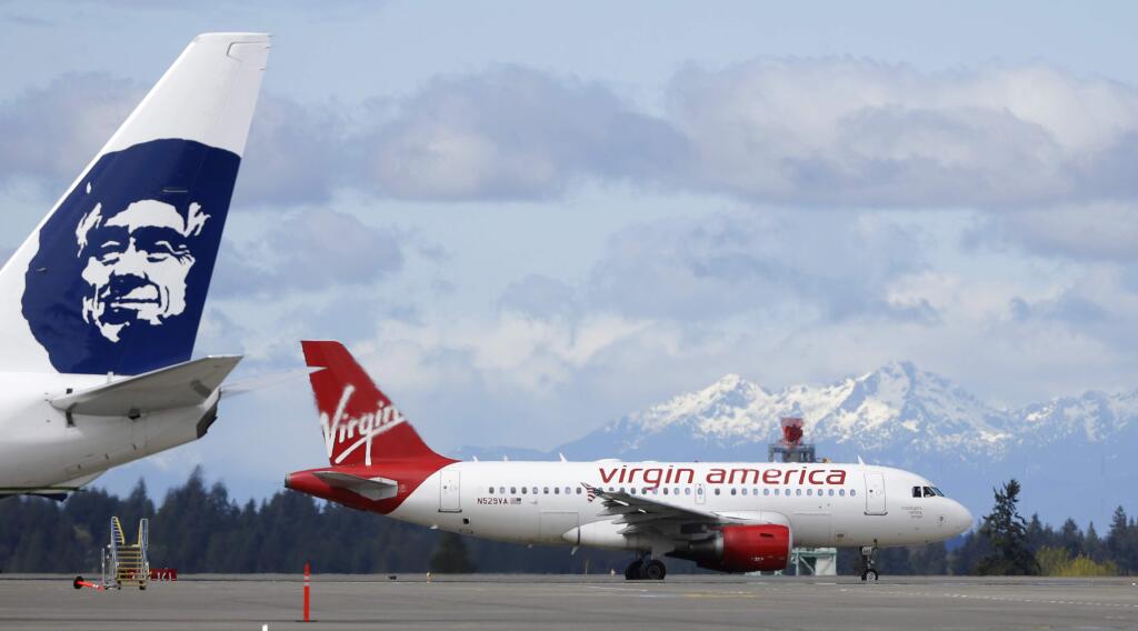 FILE - In this Monday, April 4, 2016, file photo, a Virgin America plane taxis past an Alaska Airlines plane waiting at a gate, at Seattle-Tacoma International Airport in Seattle. Alaska said Wednesday, March 22, 2017, that it will retire the Virgin brand, probably in 2019. Alaska announced in 2016, that it was buying Virgin, but CEO Brad Tilden held out hope to Virgin fans that he might keep the Virgin America brand, and run it and Alaska as separate airlines under the same corporate umbrella. (AP Photo/Ted S. Warren, File)