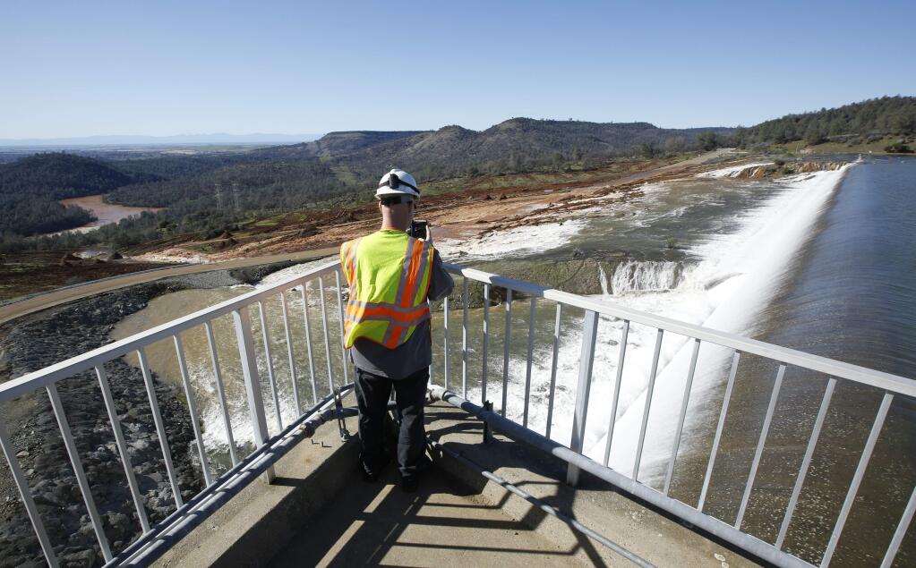 Jason Newton of the state Department of Water Resources takes a picture of water going over the emergency spillway at Oroville Dam on Saturday. (RICH PEDRONCELLI / Associated Press)
