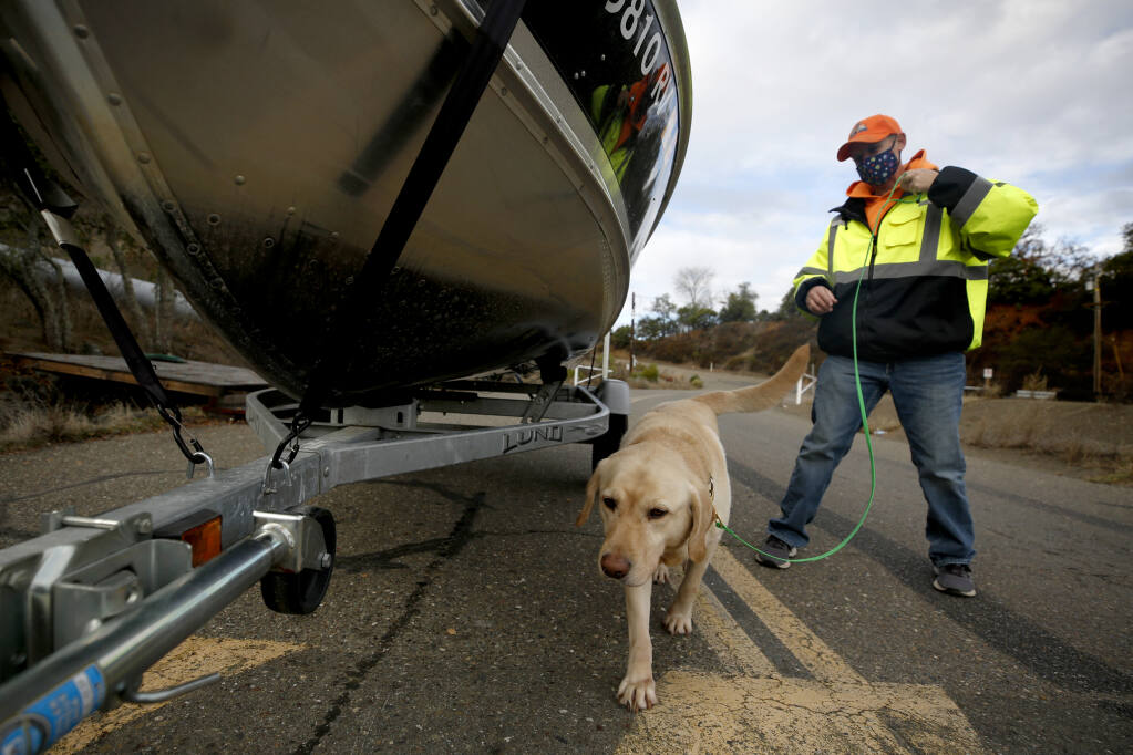 Beth Steinkraus leads the dog, Tugboat, around a boat to sniff for quagga and zebra mussels during an inspection at the boat ramp at Lake Sonoma north of Healdsburg on Tuesday, Dec. 15, 2020. (Beth Schlanker/ The Press Democrat)