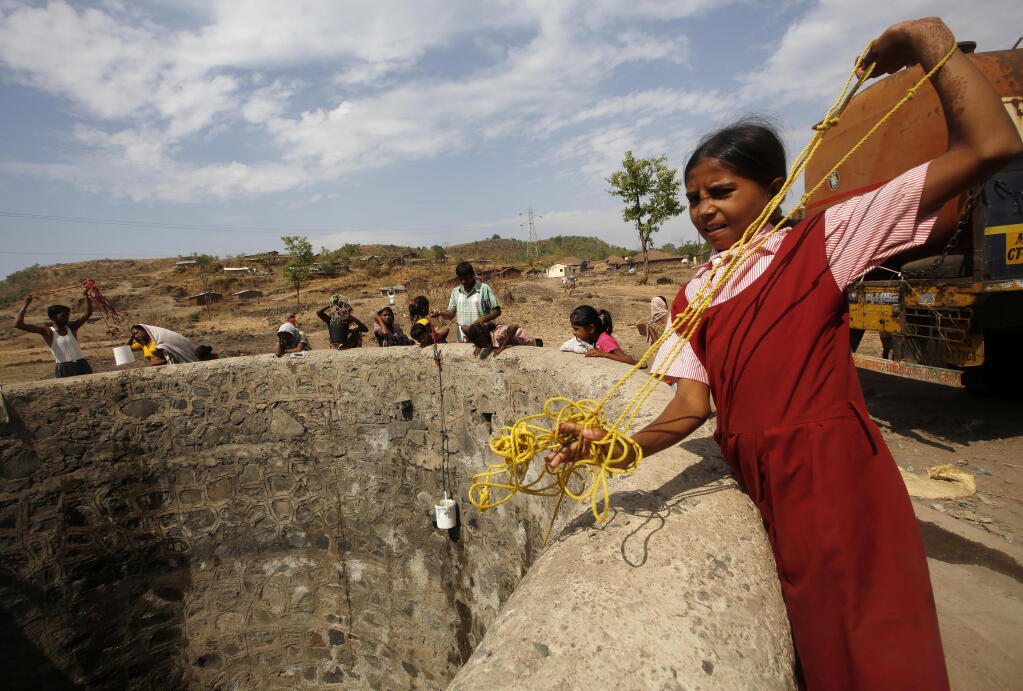 FILE - In this May 4, 2016, file photo, a girl wearing her school uniform pulls a rope attached to a bucket as she tries to draw water after a tanker emptied water into a dried up well at Umber Maal village in Thane district in Maharashtra state, India.  Climate change could push more than 200 million people to move within their own countries in the next three decades and create migration hotspots unless urgent action is taken in the coming years to reduce global emissions and bridge the development gap, a World Bank report has found. The report published on Monday, Sept. 13, 2021 examines how long-term impacts of climate change such as water scarcity, decreasing crop productivity and rising sea levels could lead to millions of what the report describes as “climate migrants” by 2050. (AP Photo/ Rajanish Kakade, File)