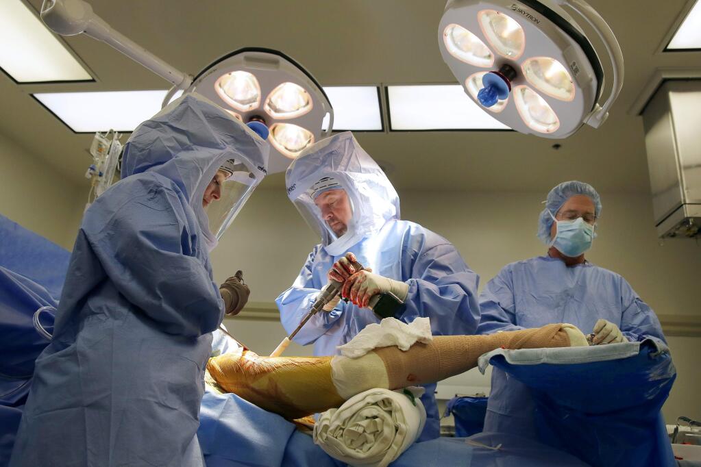 Orthopedic surgeon Kevin Howe, MD, center, physician assistant Natalie Carlberg, left, and scrub technician Gordon Henry, right, perform a hip replacement surgery on Lee Olibas at Santa Rosa Memorial Hospital on Friday, July 18, 2014. (Conner Jay/The Press Democrat)