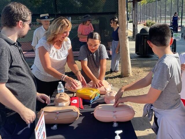 Tami Bender of Healthy Petaluma’s HeartSafe Community Program (center, in white) demonstrates CPR technique during an unveiling event for the city’s newly installed AED station at Leghorns Park on Tuesday, Aug. 22, 2023. (Photo courtesy Healthy Petaluma)