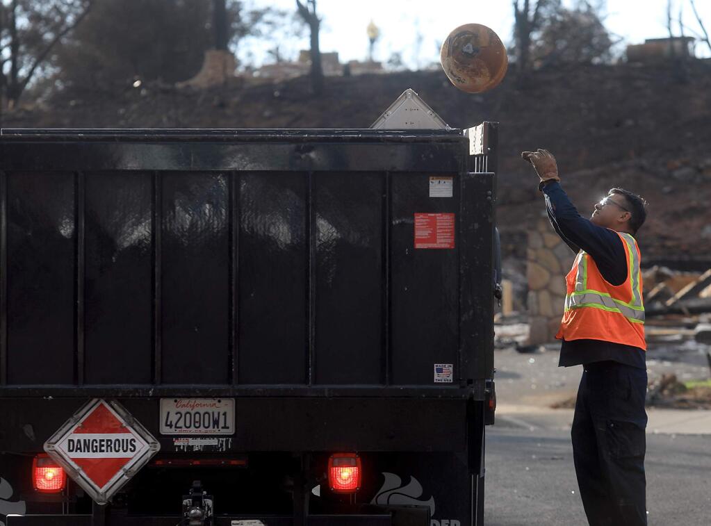 A contracted worker with the EPA tosses a propane tank for disposal during the ongoing Tubbs fire hazardous materials cleanup in Fountaingrove, Thursday Nov. 2, 2017 in Santa Rosa. (Kent Porter / The Press Democrat) 2017