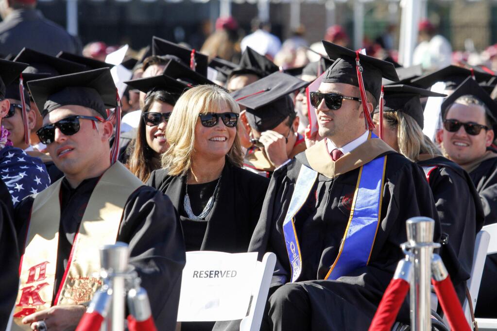 In this Saturday, May 20, 2017 photo, provided by Chapman University, Judy O'Connor, center, sits with her son, MBA graduate Marty O'Connor, during commencement at Chapman University in Orange, Calif. Chapman University gave a surprise honorary degree to Judy O'Connor, mother of Marty O'Connor a quadriplegic student after she attended every class and took notes for him while he earned a master's degree. (Chapman University via AP)