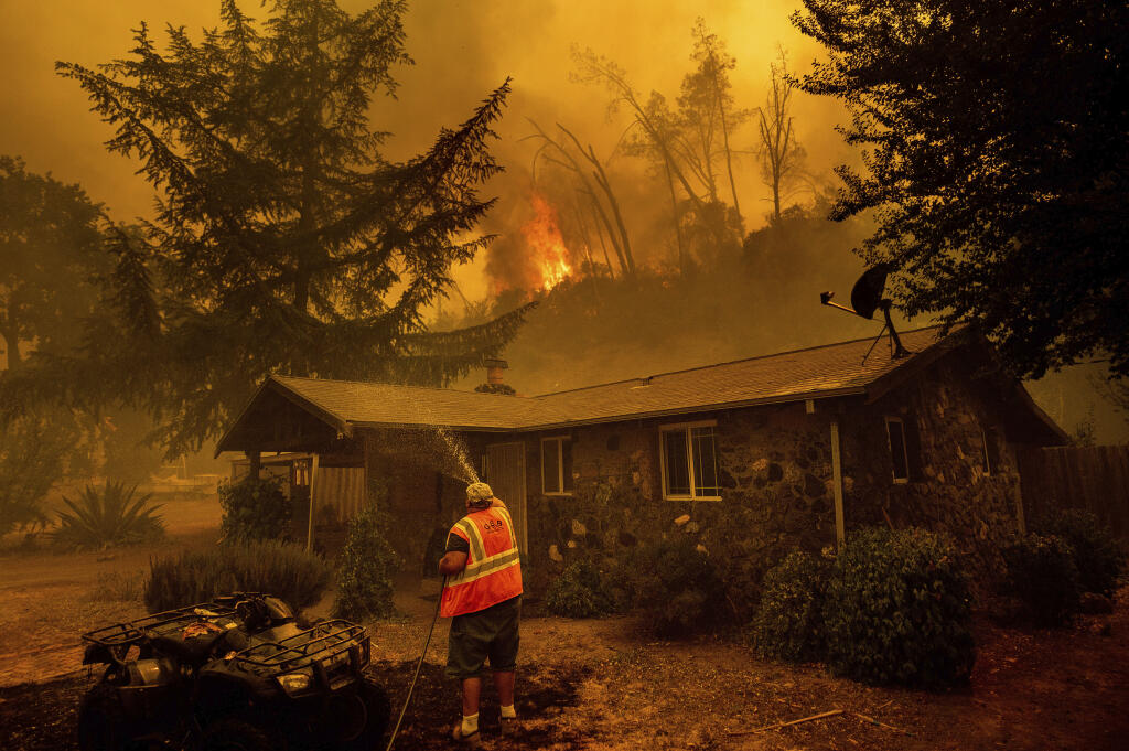 FILE - In this Aug. 18, 2020, file photo, Jerry Kuny sprays water on a home as flames from the LNU Lightning Complex fires approach in unincorporated Napa County, Calif. This home remained standing as the main front passed although the fire went on to destroy multiple residences.  (AP Photo/Noah Berger, File)