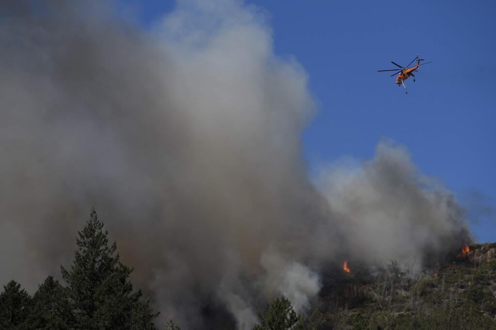 A helicopter flies over a wildfire Thursday, Oct. 12, 2017, near Calistoga. Officials say progress is being made in some of the largest wildfires burning in Northern California but that the death toll is almost sure to surge. (AP Photo/Jae C. Hong)