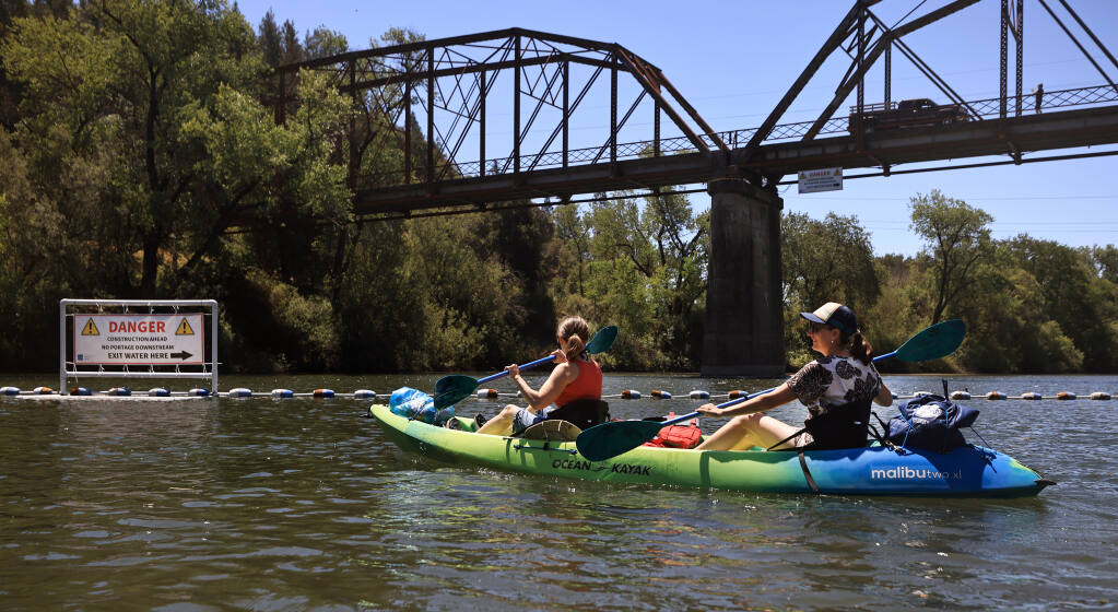 Laura Duffy, left, of Sonoma and Jodi Wilson of Petaluma, kayak upstream from a sign warning boaters not to go down stream from the Wohler Bridge due the replacement of the rubber dam that can only be done during summers low flow on the Russian River, Friday, June 25, 2021 near Forestville.  (Kent Porter / The Press Democrat) 2021