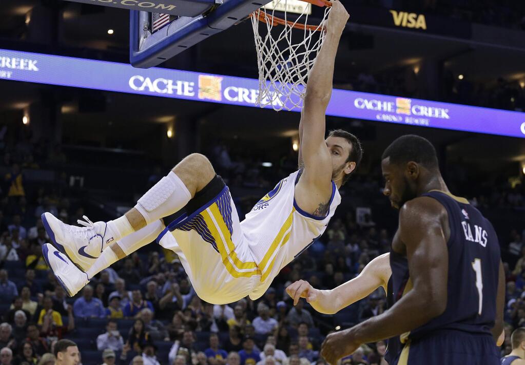 Golden State Warriors' Andrew Bogut hangs on the rim after scoring against the New Orleans Pelicans during the second half of a game Thursday, Dec. 4, 2014, in Oakland. At right is New Orleans' Tyreke Evans (1). (AP Photo/Ben Margot)
