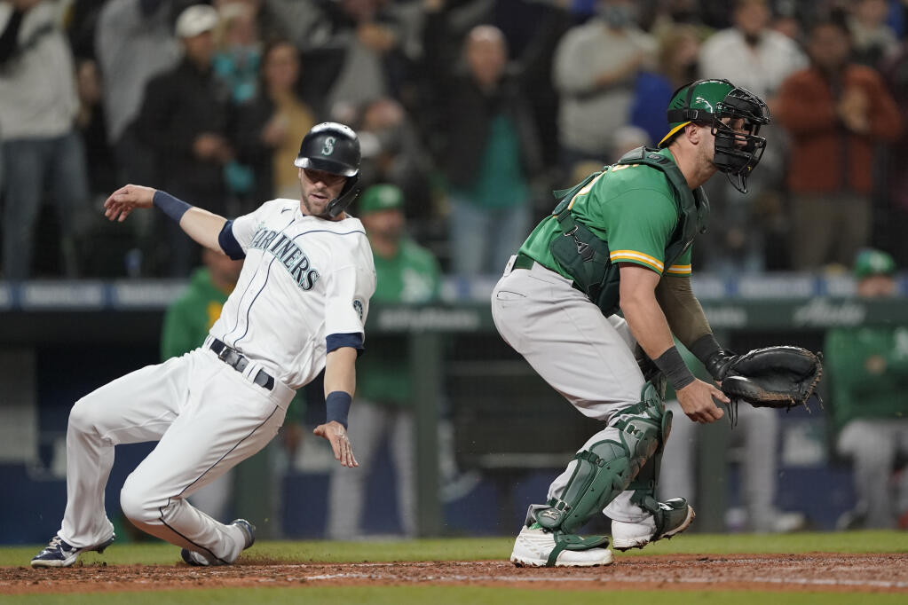 The Seattle Mariners’ Mitch Haniger, left, scores past Oakland Athletics catcher Yan Gomes on a two-RBI double hit by Jarred Kelenic during the sixth inning on Wednesday, Sept. 29, 2021, in Seattle. (Ted S. Warren / ASSOCIATED PRESS)