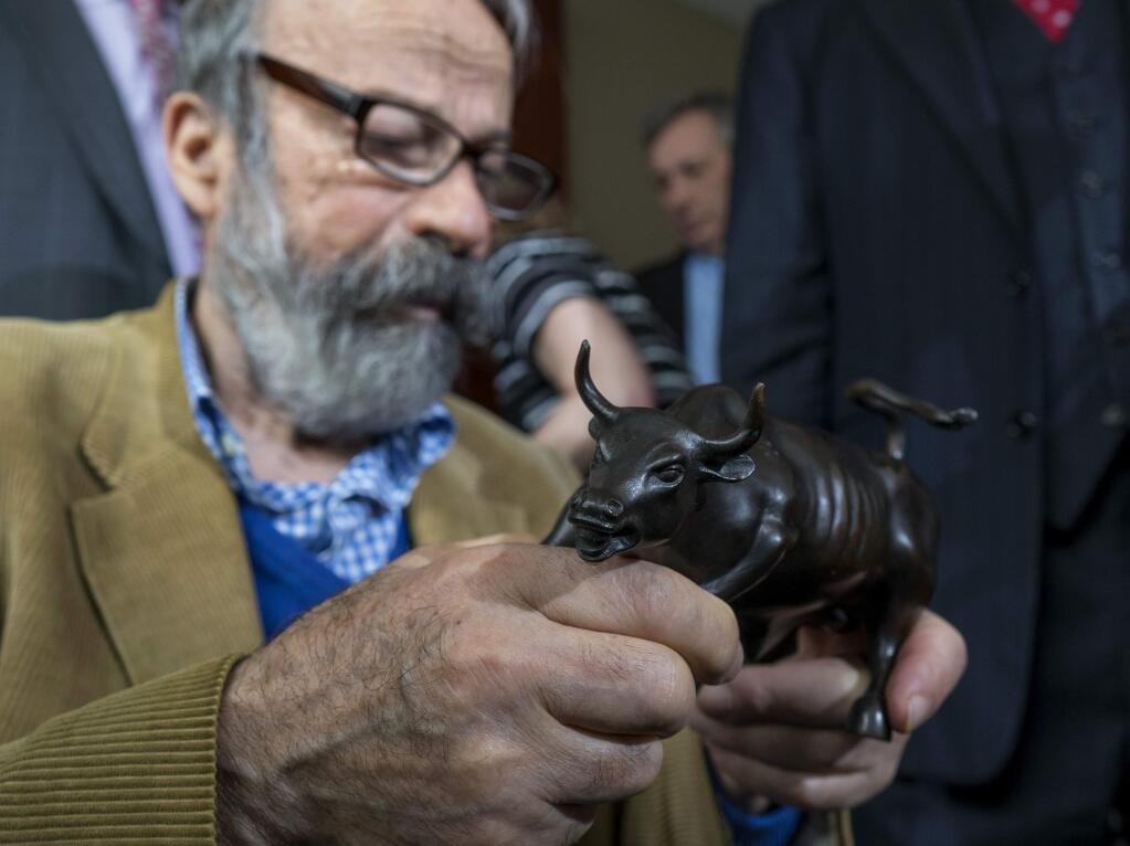 Sculptor Arturo Di Modica holds a model of Charging Bull, the depiction of the full size piece he created that draws thousands of visitors in lower Manhattan, during a news conference Wed., April 12, 2017, in New York. Di Modica and his attorneys announced at the news conference that he's challenging city officials who issued a permit for 'Fearless Girl,' a bronze statue that faces the bull sculpture on the same cobble stone island in the street, and has drawn worldwide attention. (AP Photo/Craig Ruttle)