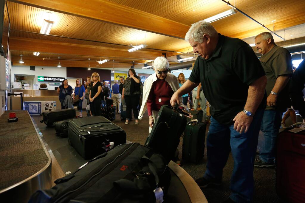 Former Santa Rosa resident Tom McGee, right, now of Peoria, Illinois, helps Marlene Miller of Tucson, Arizona pull her suitcase off the single luggage conveyor that currently services all four airlines flying into Charles M. Schulz-Sonoma County Airport in Santa Rosa, California, on Tuesday, July 11, 2017. Airport officials are planning to double the size of Gate 2, add more parking spaces and build a new 28,000 square foot terminal in the future. (Alvin Jornada / The Press Democrat)