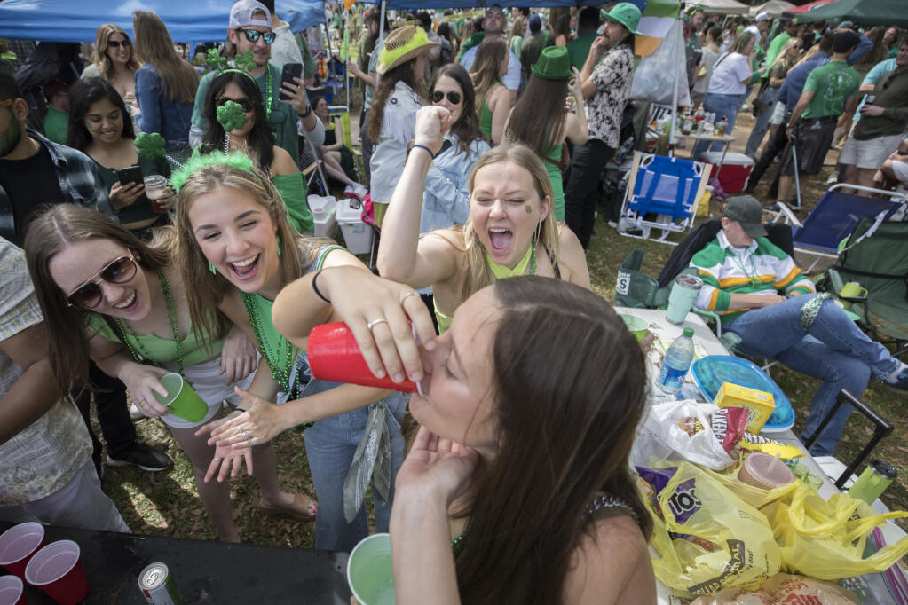 Julie Hensley, center, pumps her fist as her friend Ally Womble, bottom center, drinks a drink while partying in a square during in the St. Patrick's Day parade, Friday, March 17, 2023, in historic downtown Savannah, Ga. After nearly two centuries, the Irish holiday has become Savannah's most profitable tourist draw and street party for hundreds of thousands of locals and visitors. (AP Photo/Stephen B. Morton)