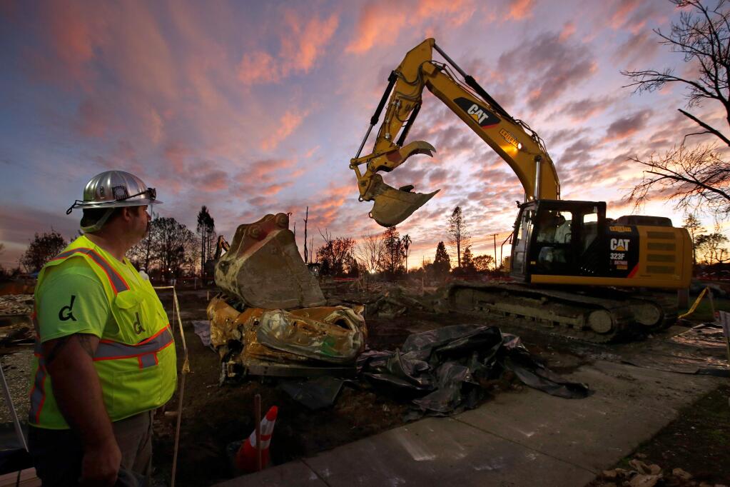 Laborer James Clowers, left, of Ghilotti Construction Company looks on while an excavator crew removes debris from a property on Pine Meadow Drive in the Coffey Park neighborhood of Santa Rosa, California on Tuesday, November 28, 2017. (Alvin Jornada / The Press Democrat)