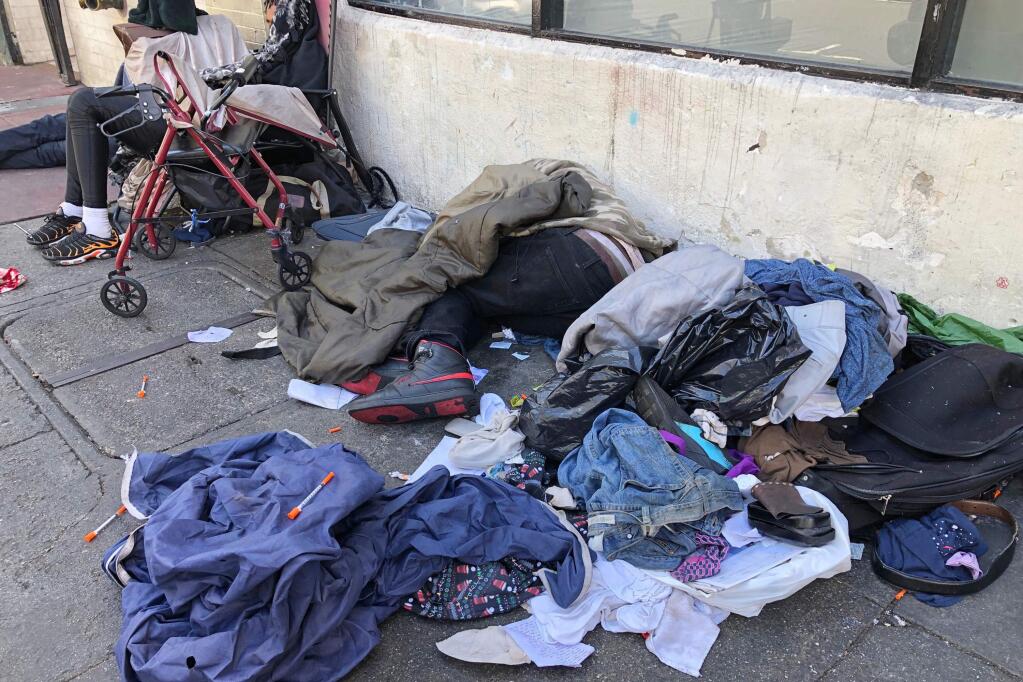 FILE - In this July 25, 2019, file photo, sleeping people, discarded clothes and used needles are seen on a street in the Tenderloin neighborhood in San Francisco. (AP Photo/Janie Har, File)