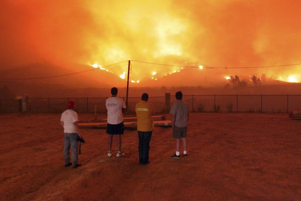 FILE - In this Nov. 15, 2008 file photo residents look on as a wind driven Santa Ana fire threatens homes, in Yorba Linda, Calif. Wildfire lawsuits have typically targeted electric utilities and their downed powerlines that ignite the blaze, but some recent lawsuits have also focused on the public water systems that are supposed to provide water to fight the flames. One lawsuit stemming from a 2008 fire forced the Yorba Linda Water District to pay $70 million to 12 homeowners. (AP Photo/Richard Vogel, File)