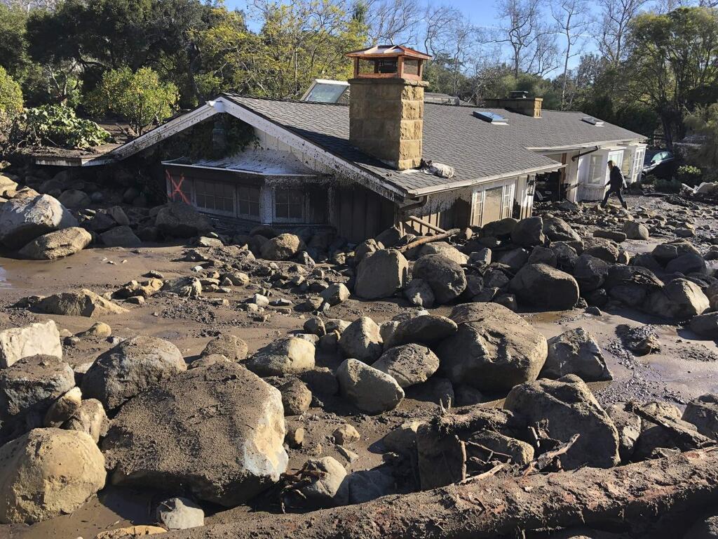 FILE - In this Jan. 10, 2018, file photo provided by Santa Barbara County Fire Department, Kerry Mann navigates the large boulders and mudflow that destroyed the home of her friend in Montecito, Calif. Authorities are urging people living in an area devastated by mudslides to evacuate ahead of a strong Pacific storm that forecasters say is likely to bring an extended period of rain and the threat of flooding and debris flows. Santa Barbara County issued a mandatory evacuation order Monday, March 19, 2018, affecting about 30,000 people, including the community of Montecito, where 21 people were killed by a massive mudslide in January. (Mike Eliason/Santa Barbara County Fire Department via AP, File)