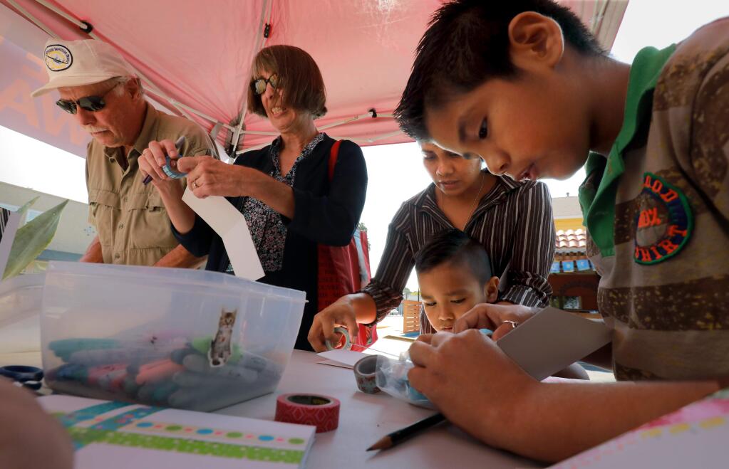From left, locals Bob and Sue Vargas write cards for loved ones along with Maria, Giovani, 5, and Maurico Lopez, 10, at the Love Letters Artwalk in Boyes Hot Springs on Saturday, September 9, 2017. (John Burgess/The Press Democrat)